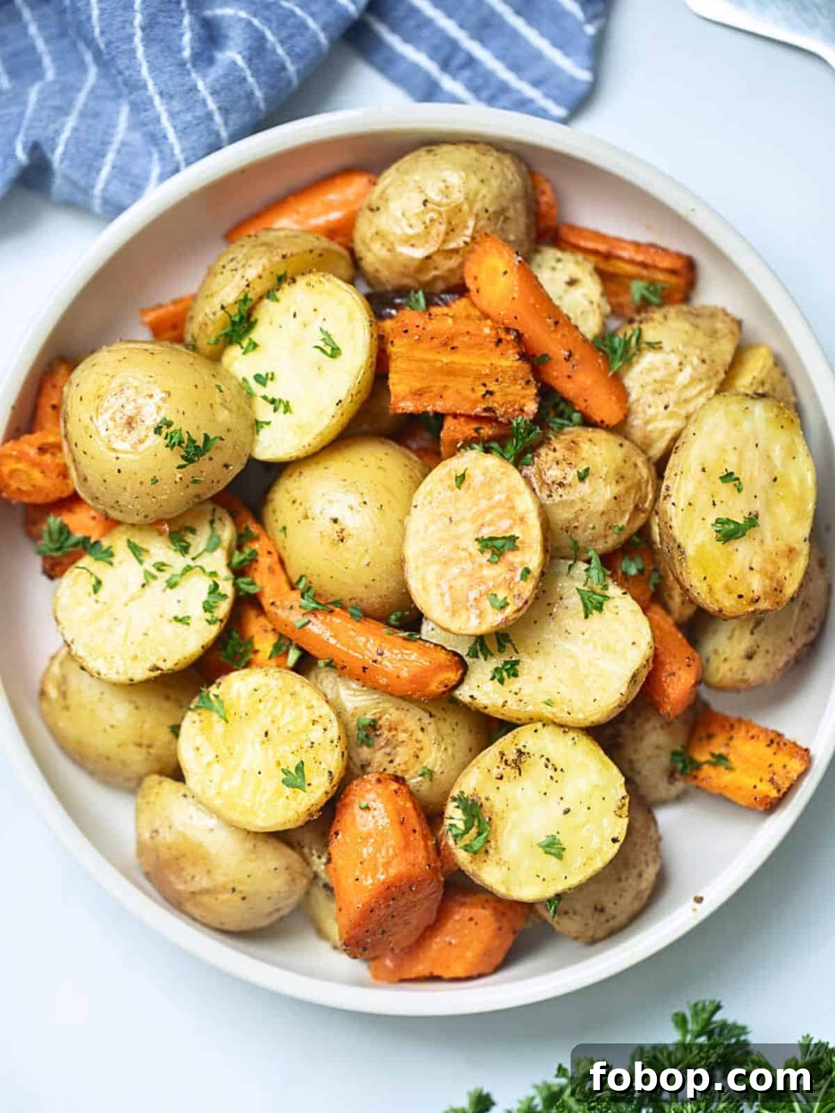 Roasted Potatoes and Carrots Roasted potatoes and carrots in white serving bowl next to fresh parsley.