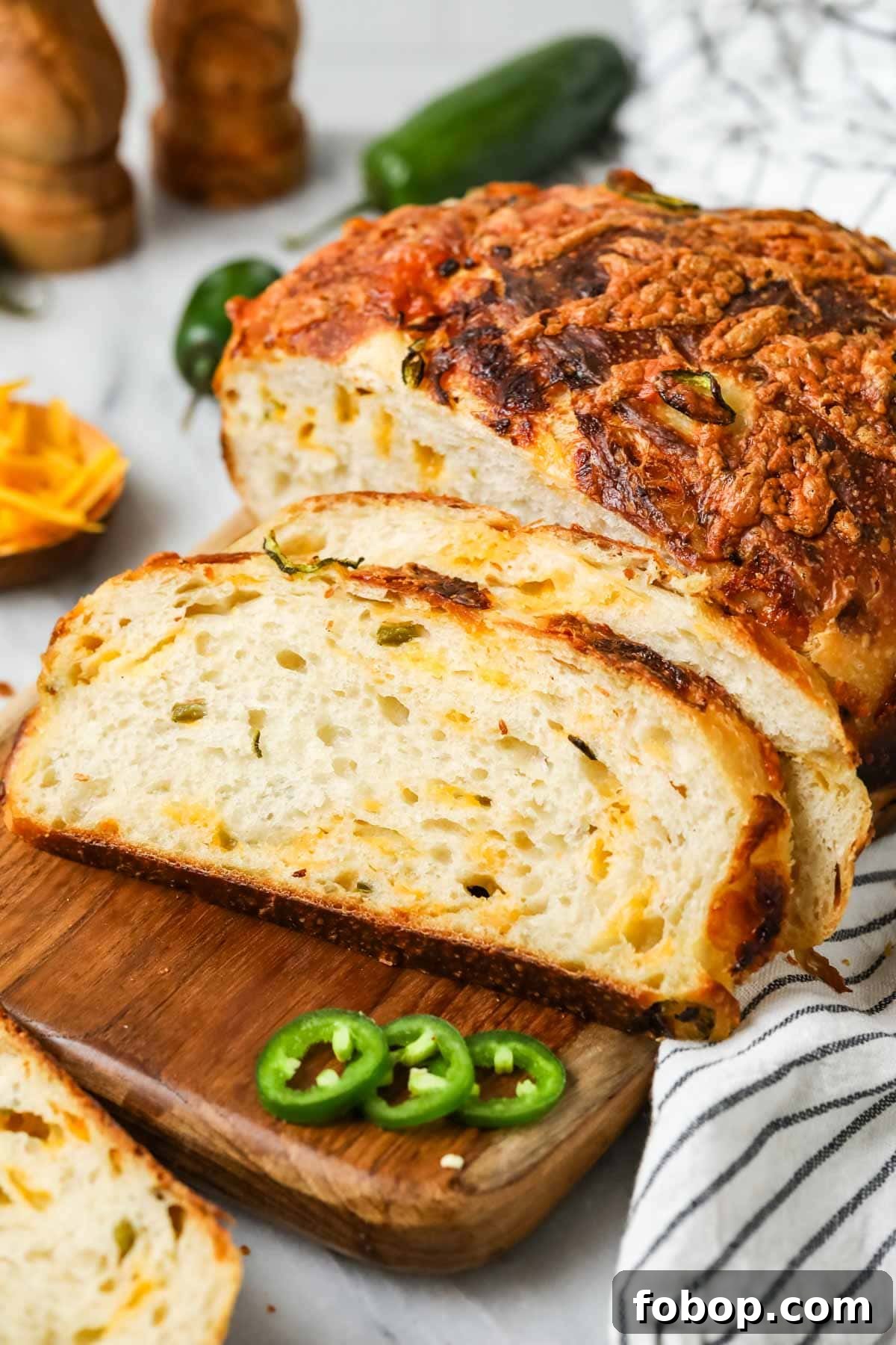 Slices of sourdough cheddar jalapeno bread resting beside the loaf on a cutting board.