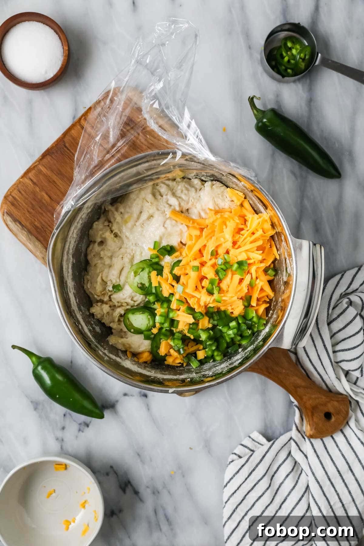 Overhead view of a mixing bowl with sourdough bread dough topped with shredded cheese and jalapenos.