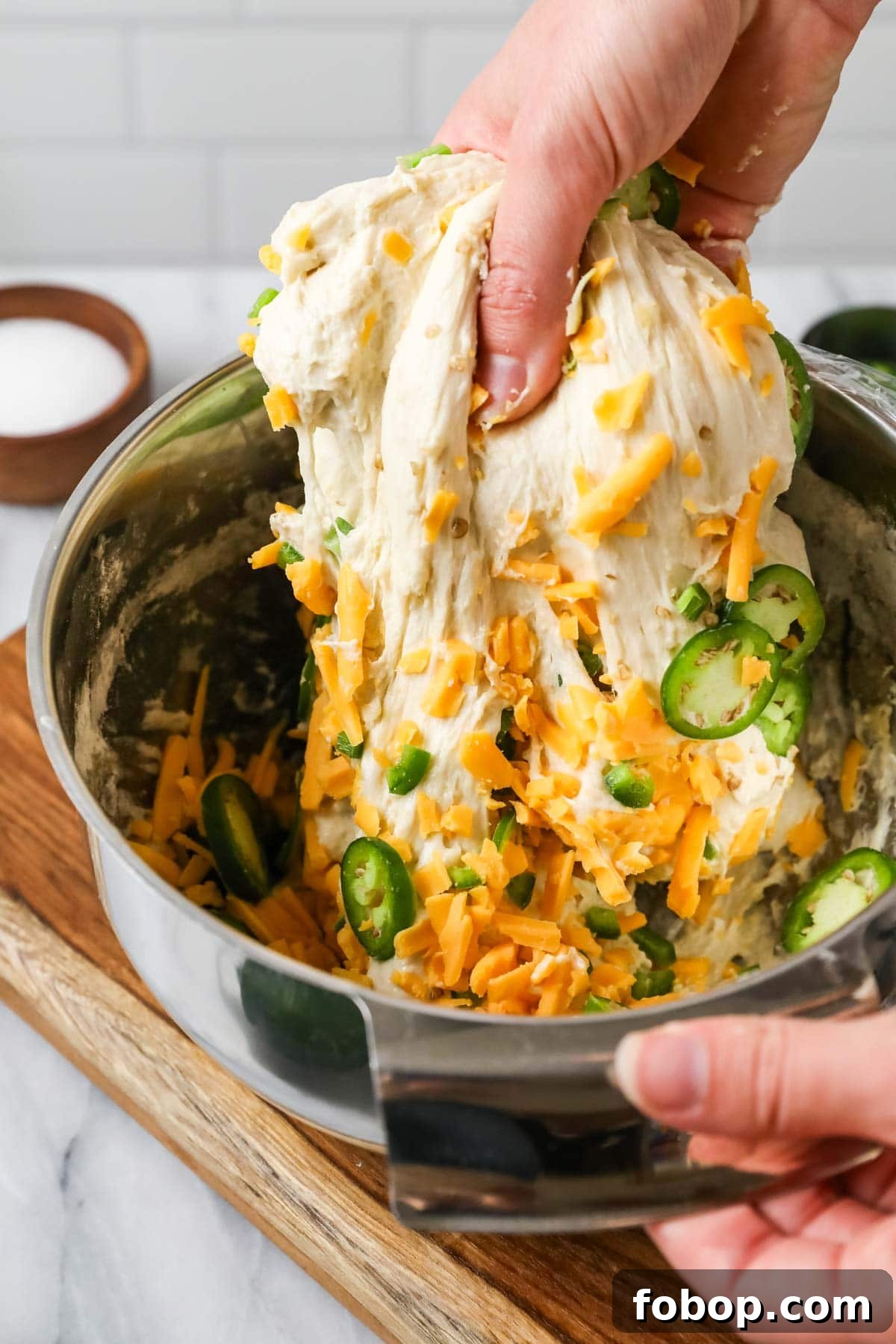 Hands stretching a cheddar jalapeno dough in a bowl.