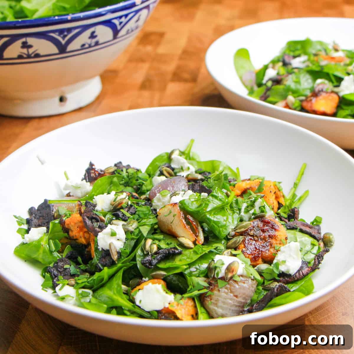 Spinach & Butternut Squash Salad with Smoky Mushroom Bacon and Vegan Feta 2 Photo of a bowl of vegan spinach and squash salad with another portion in a bowl behind and large serving salad bowl to the side.