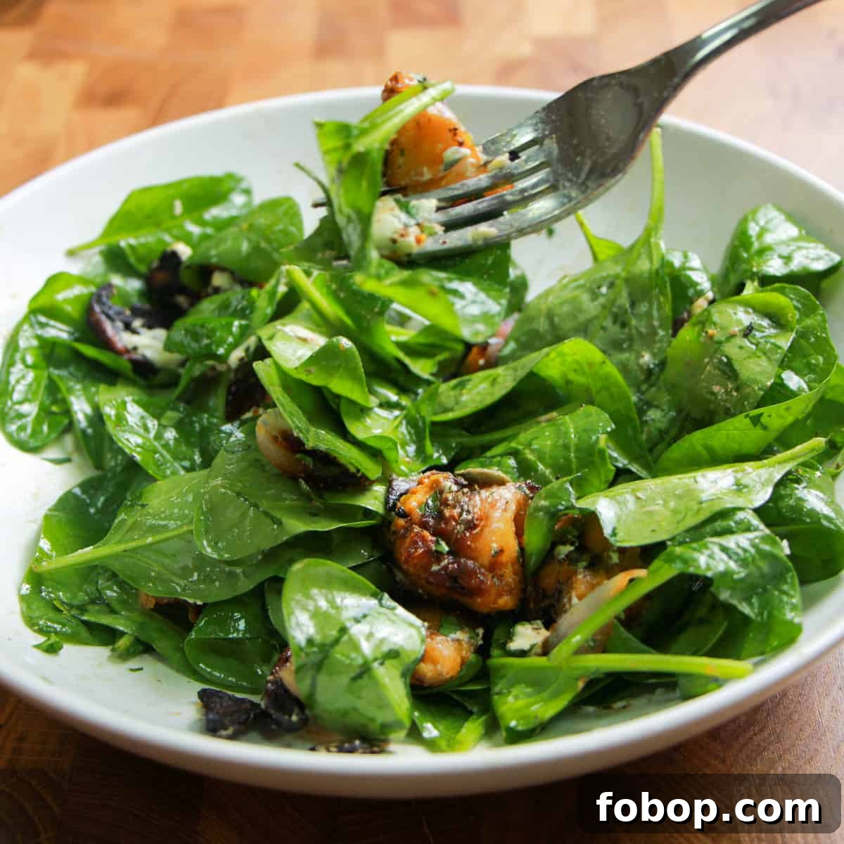 Spinach & Butternut Squash Salad with Smoky Mushroom Bacon and Vegan Feta 11 bowl of spinach, squash and mushroom bacon salad mixed with dressing and a fork digging in.