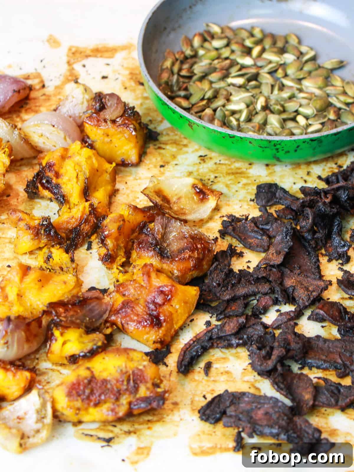 Spinach & Butternut Squash Salad with Smoky Mushroom Bacon and Vegan Feta 9 Photo of roasted butternut squash, red onion, mushroom bacon all on a roasting tin with a small pan of toasted pumpkin seeds.