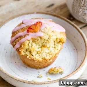 Blood Orange Coconut Muffins with Zesty Glaze 6 A single orange coconut muffin topped with an orange vanilla glaze and a small orange slice on a plate, with a bite missing.