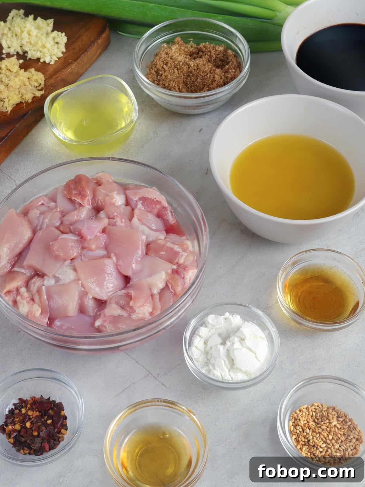 Calamansi Chicken Recipe: Tangy Citrus-Glazed Roast Chicken 3 cubed chicken thighs, calamansi juice, soy sauce, red chili flakes, brown sugar, Chinese cooking wine, garlic, ginger, cornstarch, oil, sesame seeds, green onions in bowls