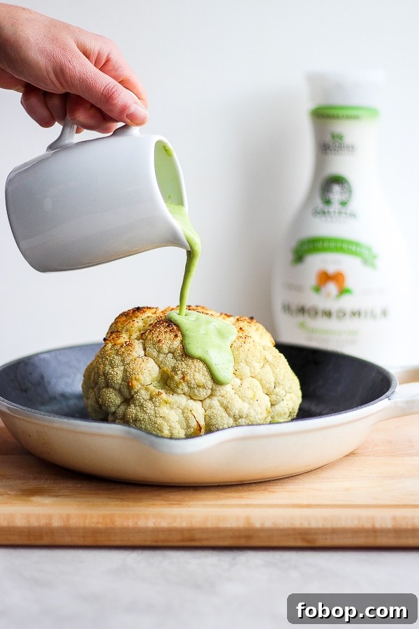 Avocado sauce being poured over a roasted head of cauliflower.