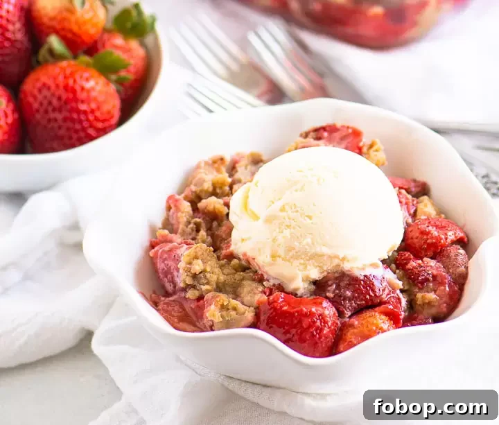 bowl of strawberry crumble topped with ice cream with a bowl of fresh strawberries in the background
