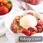 bowl of strawberry crumble topped with ice cream with a bowl of fresh strawberries in the background