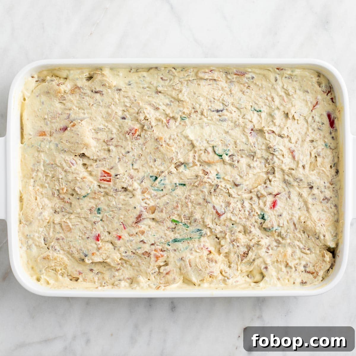 Bread, vegetables, vegan sausage, and tofu mixture combined in a baking dish.