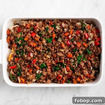 Crusty bread topped with cooked vegan sausage and vegetables in a baking dish.