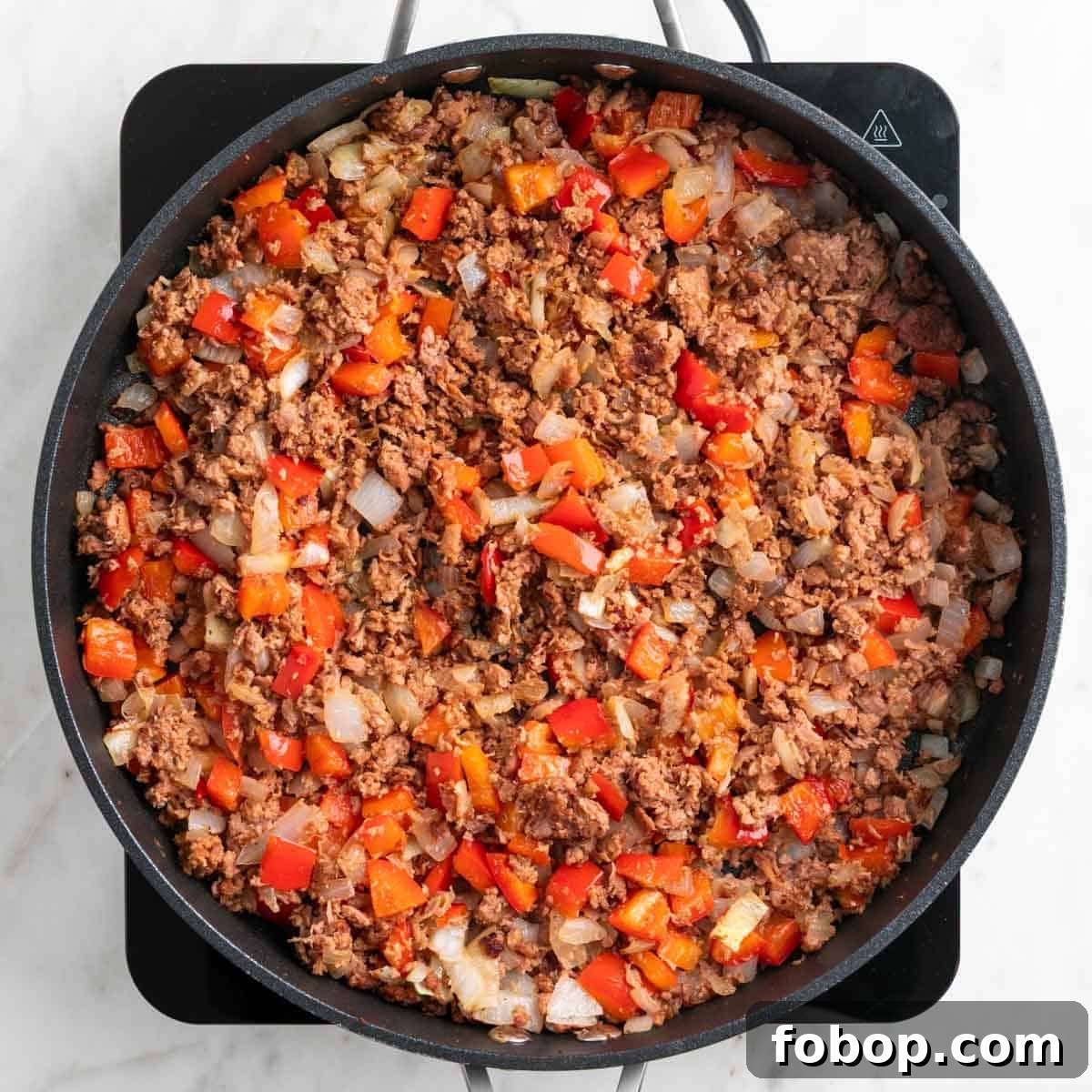 Cooked vegan sausage, onion, and red bell pepper in a skillet.