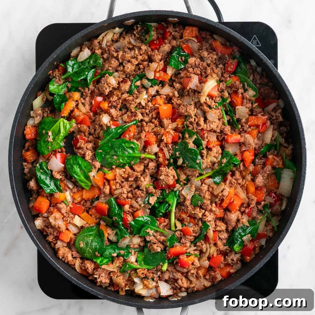 Cooked vegan sausage, onion, red bell pepper, and baby spinach in a skillet.