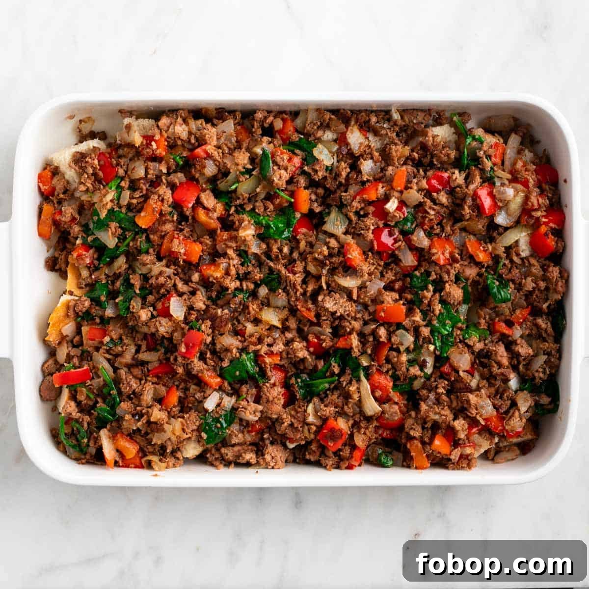 Crusty bread topped with cooked vegan sausage and vegetables in a baking dish.