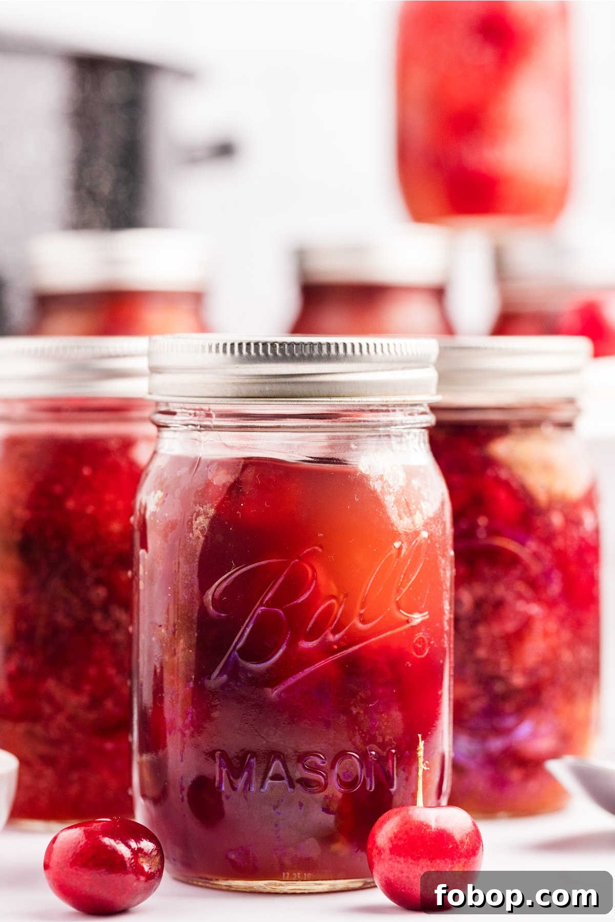 Homemade Cherry Pie Filling for Water Bath Canning: Step-by-Step Guide 2 Jars of homemade cherry pie filling with two fresh cherries in front.