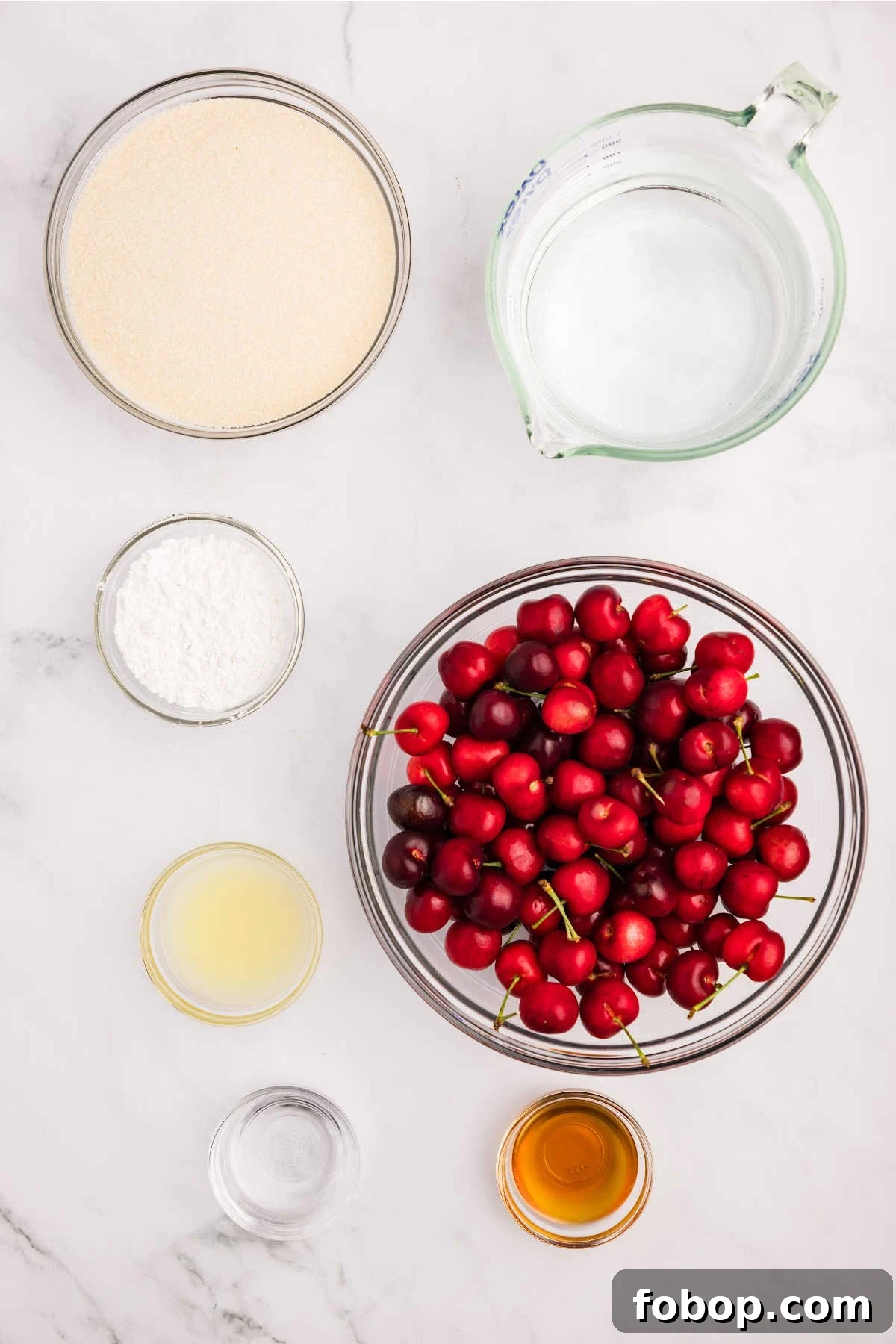 Homemade Cherry Pie Filling for Water Bath Canning: Step-by-Step Guide 3 Ingredients for cherry pie filling, including fresh cherries, sugar, water, and extracts, laid out on a marble countertop.