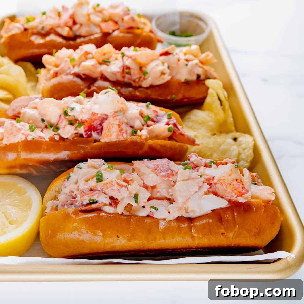 Classic Maine Lobster Roll Recipe: How to Make Authentic Lobster Rolls 11 Three lobster rolls on a try with chives, lemon and chips.