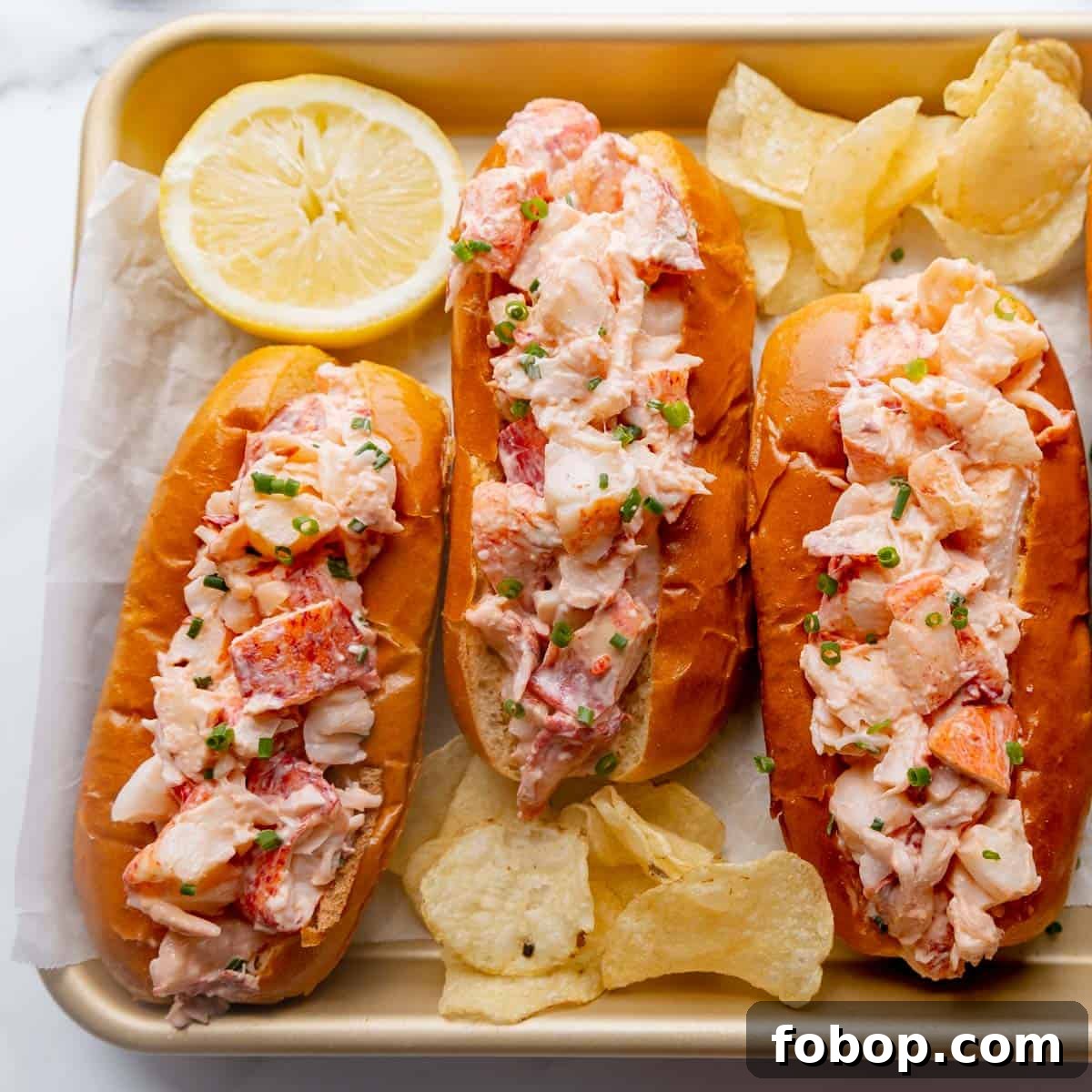 Classic Maine Lobster Roll Recipe: How to Make Authentic Lobster Rolls 12 Three lobster rolls on a tray with lemon and chips.