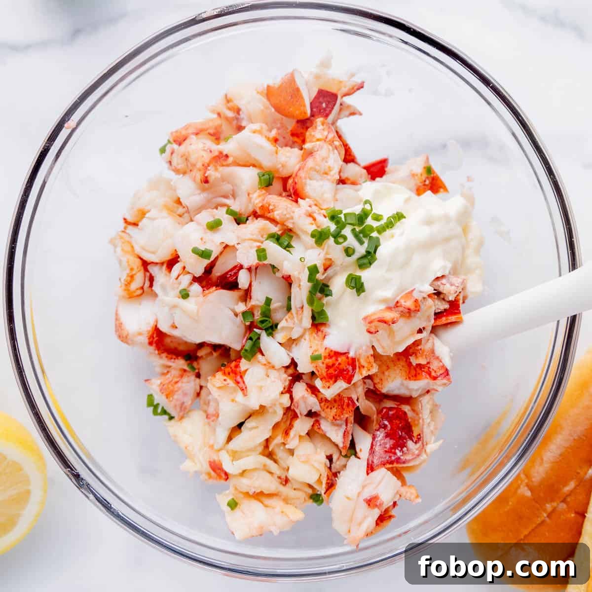 Classic Maine Lobster Roll Recipe: How to Make Authentic Lobster Rolls 5 lobster meat in a glass bowl with mayo, chives, and a white spoon.