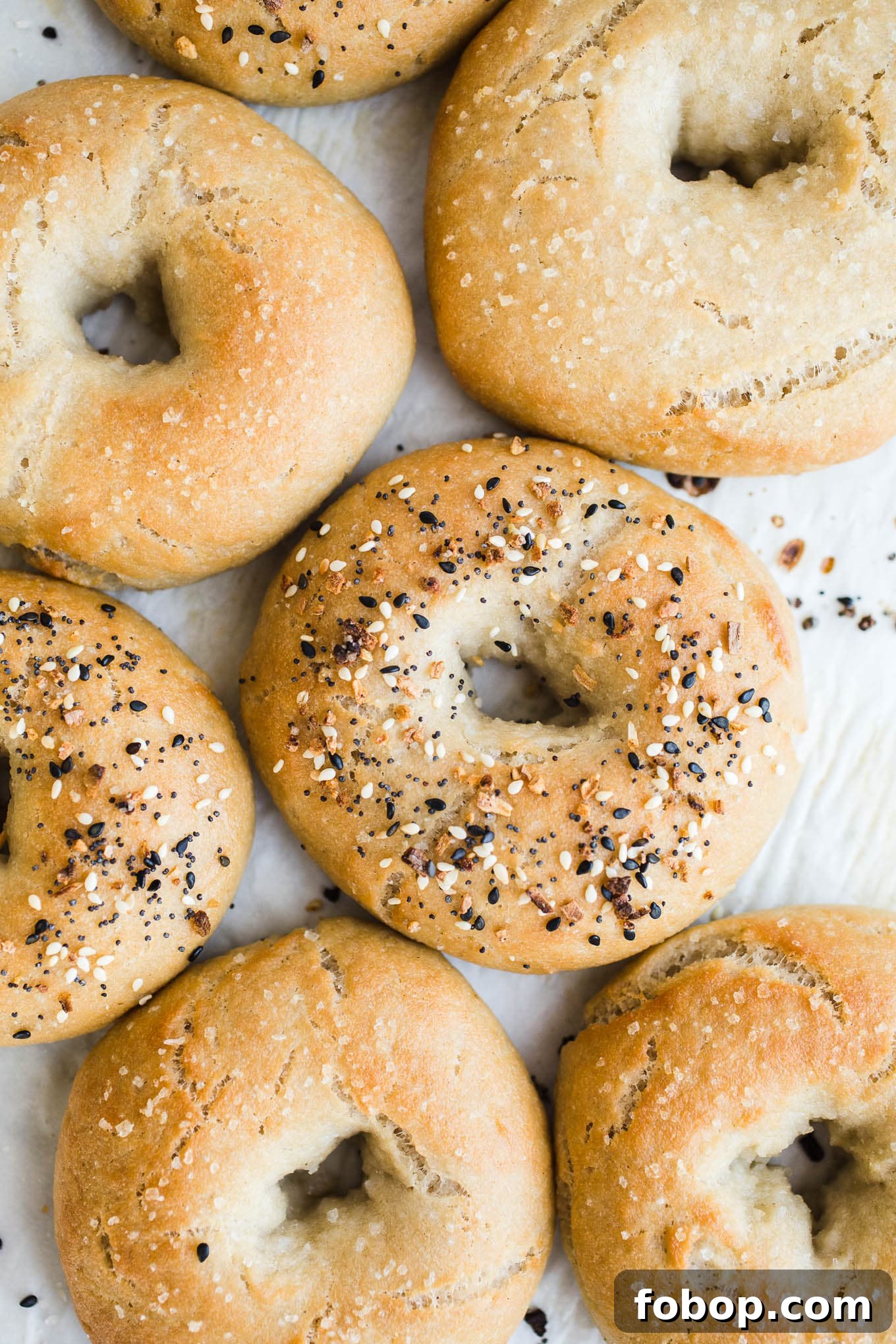 Vegan Gluten-Free Bagel Recipe: Soft Homemade Bagels 2 Bagels topped with seeds on a piece of parchment paper.