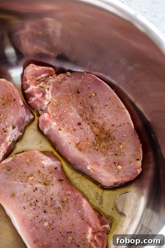 Season and sear the chops. Overhead view of three raw, seasoned pork chops cooking in an Instant Pot with oil.