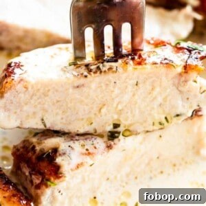 Juicy Instant Pot Pork Chops with Garlic Herb Sauce 3 Close-up image of a fork stuck through a bite of a cream-covered pork chop.
