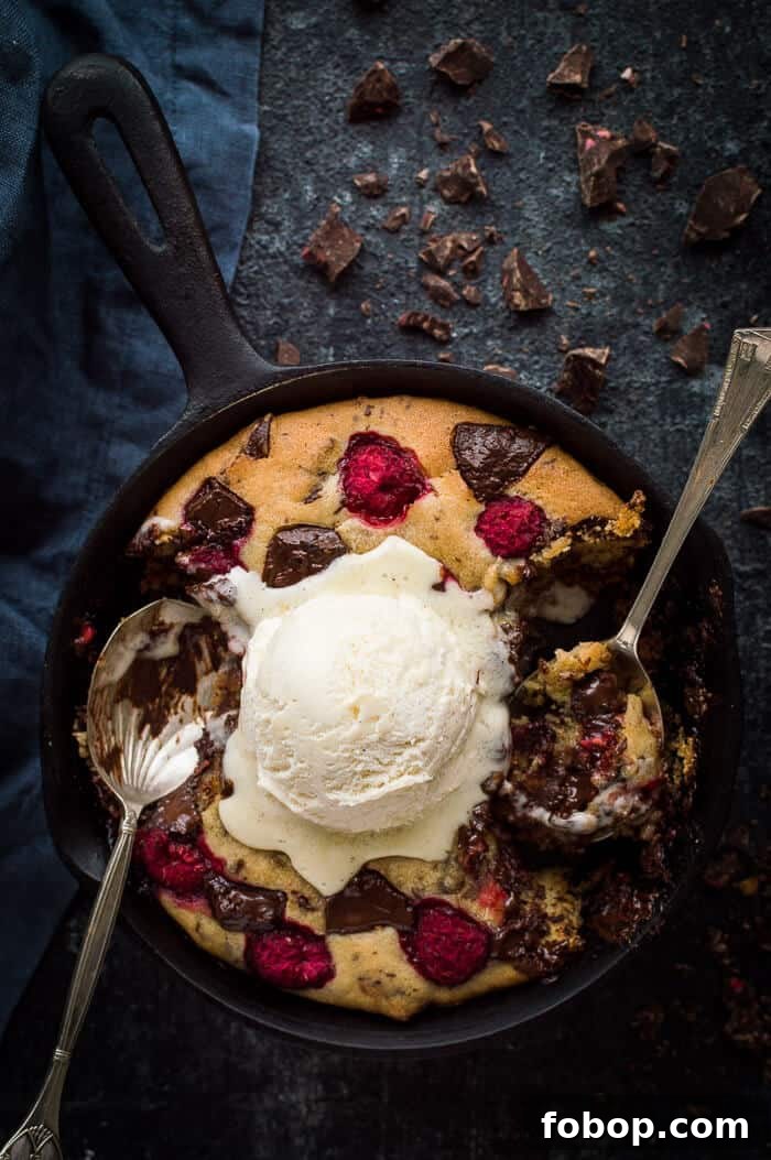Vegan Chocolate Raspberry Skillet Cookie for Two – Decadent Dessert 3 Partially eaten mini vegan chocolate raspberry skillet cookie for two topped with vanilla ice cream with two spoons on a black background.
