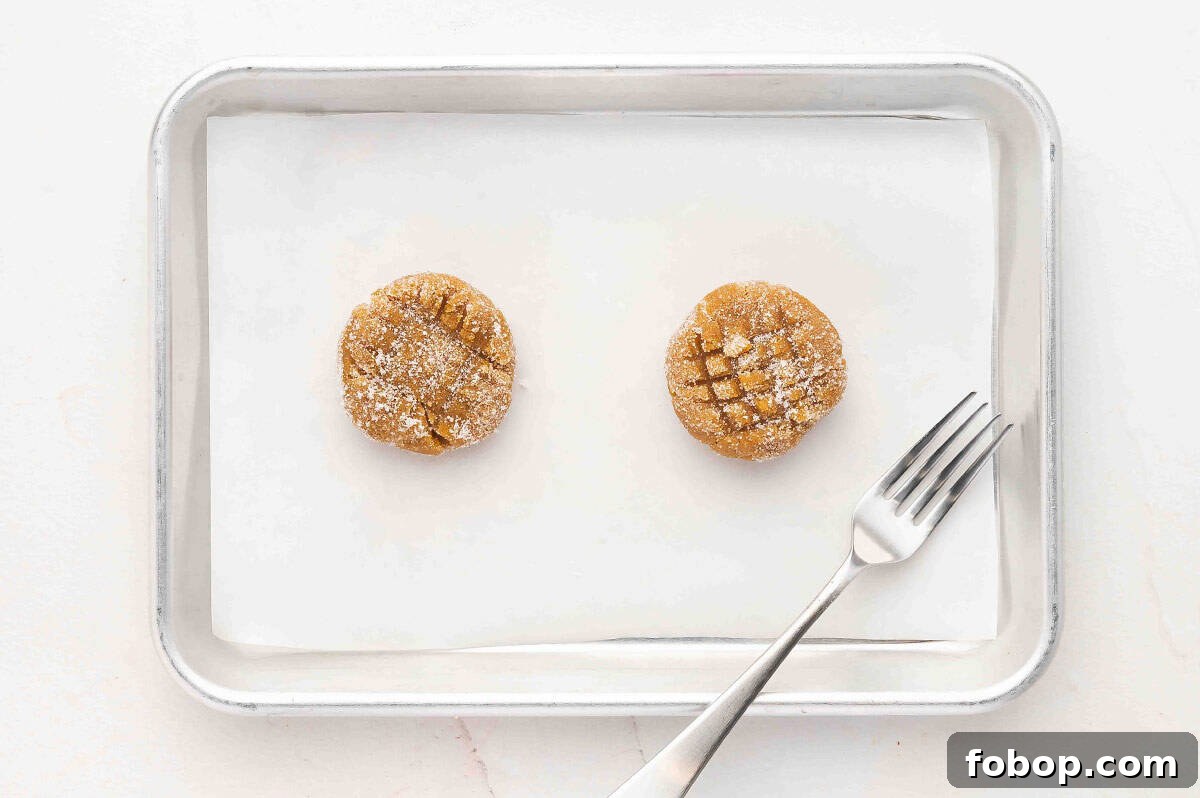 Two balls of peanut butter cookie dough on a baking sheet with a fork