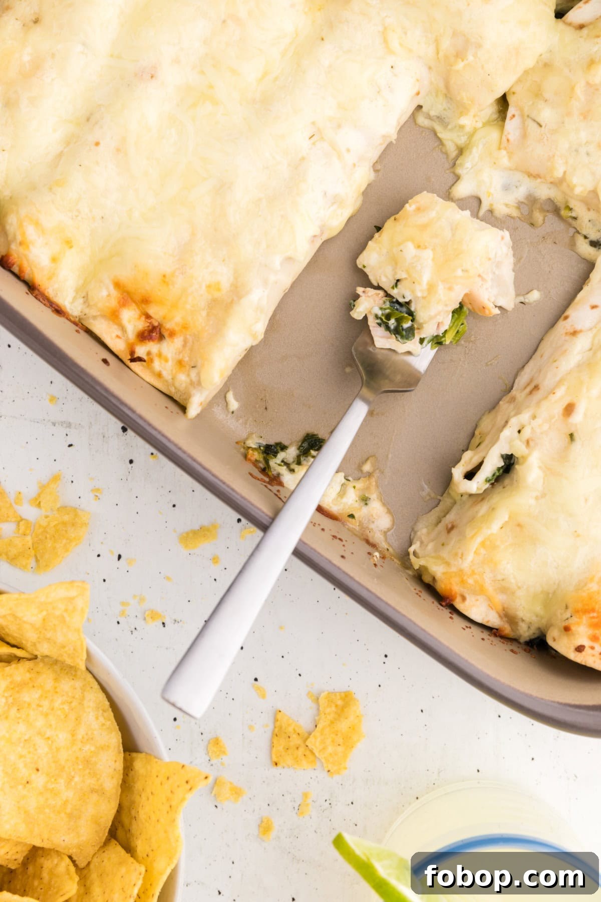 Serving a Creamy Chicken Enchilada fork full of enchilada in pan of enchiladas