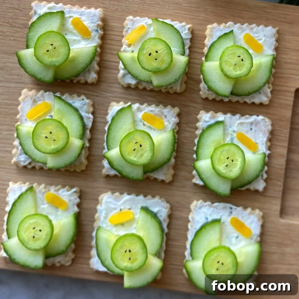 Closeup of nine crackers topped with a creamy spread, cucumber slices arranged as angels with small yellow pepper halos. They are displayed neatly on a wooden board.