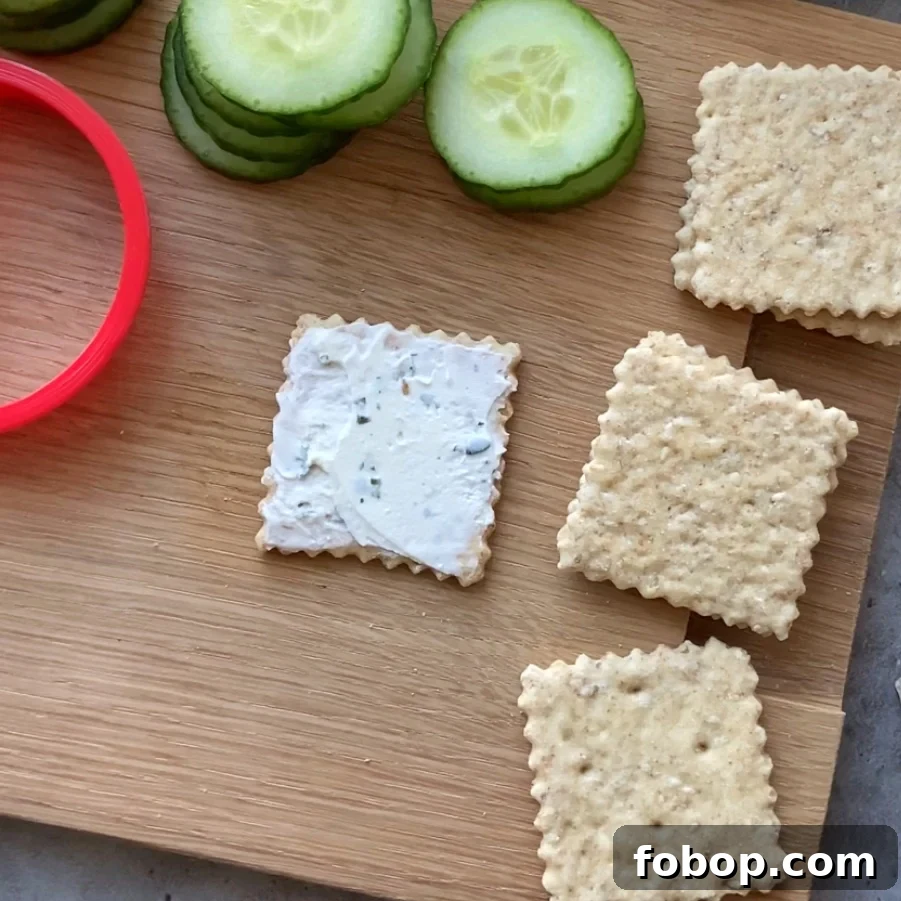 Square crackers on a wooden board, one topped with cream cheese.
