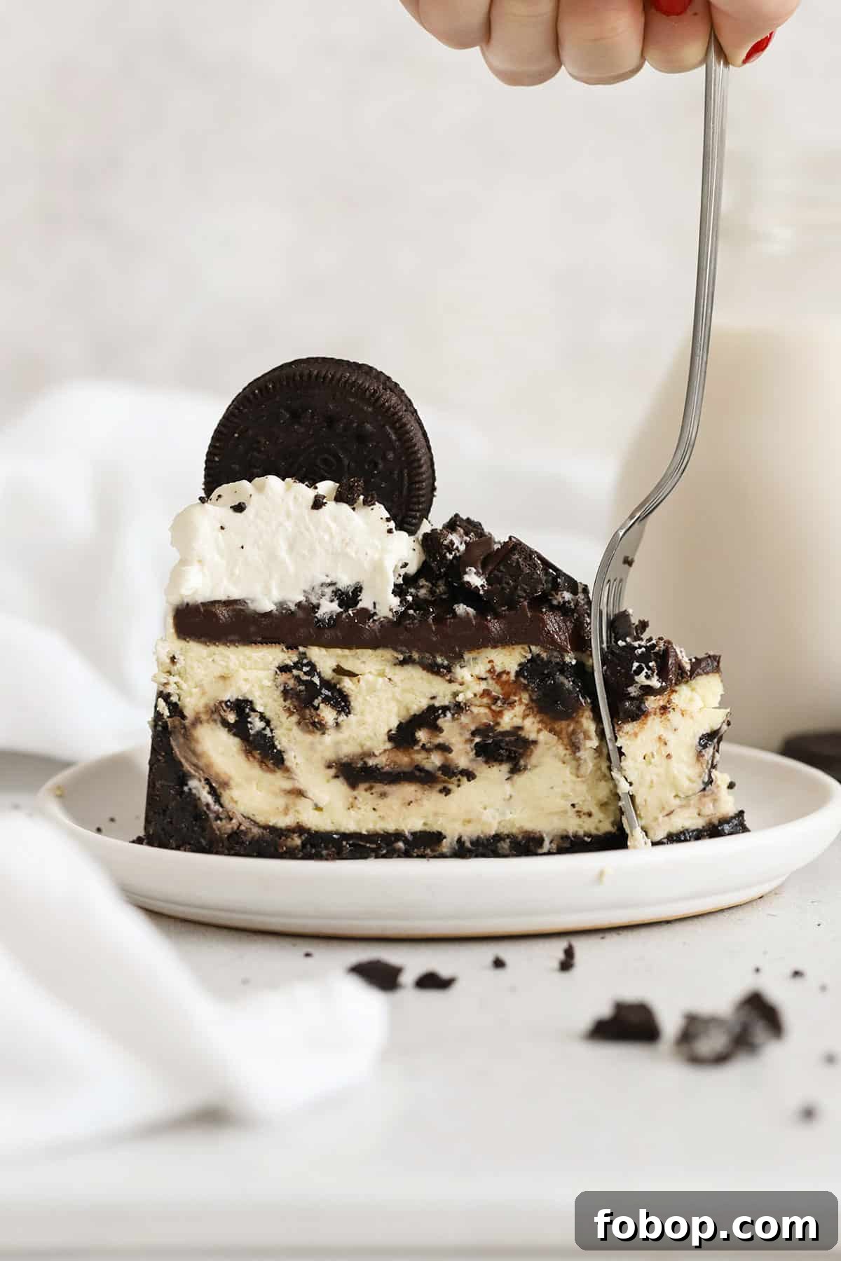fork cutting into a slice of gluten-free Oreo cheesecake on a white plate