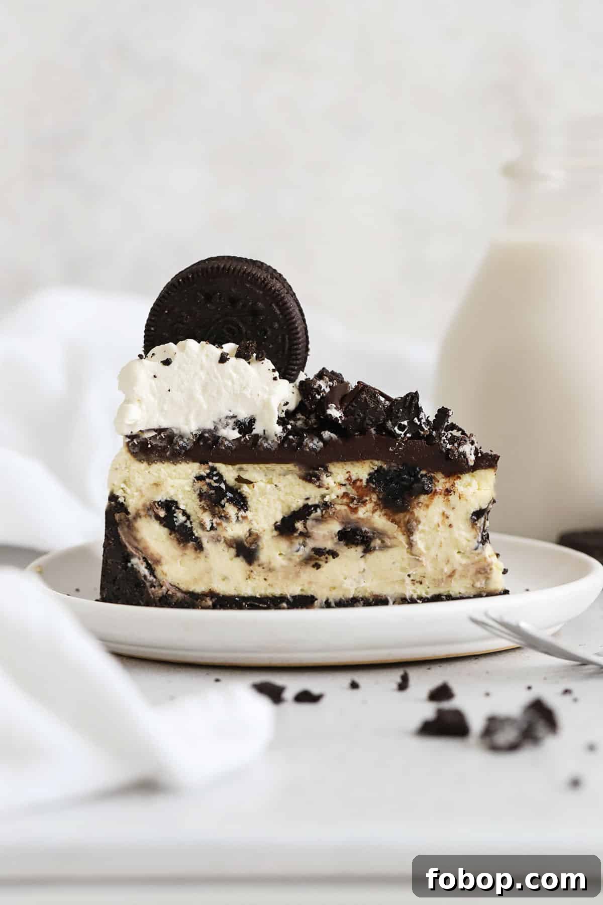 slice of gluten-free Oreo cheesecake topped with chocolate ganache, chopped Oreo cookies, and whipped cream