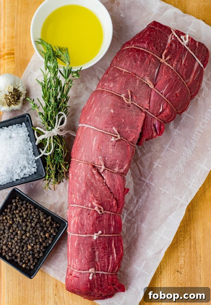 Perfect Beef Tenderloin Roast Recipe for Tender, Juicy Results 3 A raw beef tenderloin that is tied and sitting on parchment paper with salt, pepper, a bundle of rosemary and thyme and a bowl of melted butter.