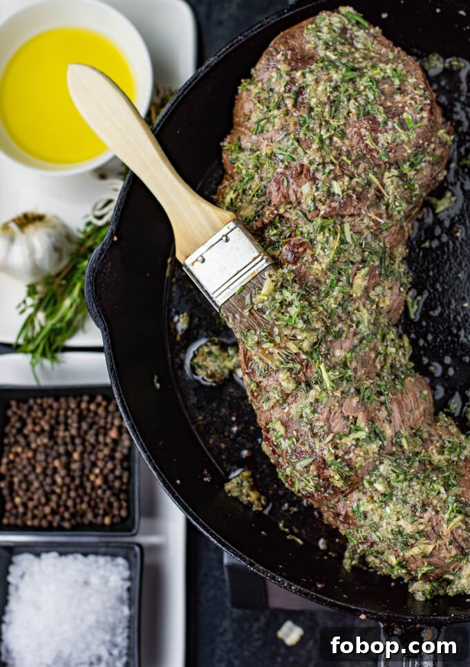 Perfect Beef Tenderloin Roast Recipe for Tender, Juicy Results 4 An uncooked beef tenderloin sits in a cast-iron skillet with a herb garlic rub smeared on it. A wooden pastry brush sits on top of it.