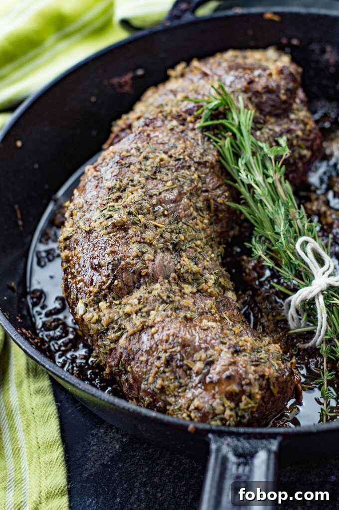 Perfect Beef Tenderloin Roast Recipe for Tender, Juicy Results 5 A cooked beef tenderloin sits in a cast iron pan with a bundle of fresh rosemary next to it.