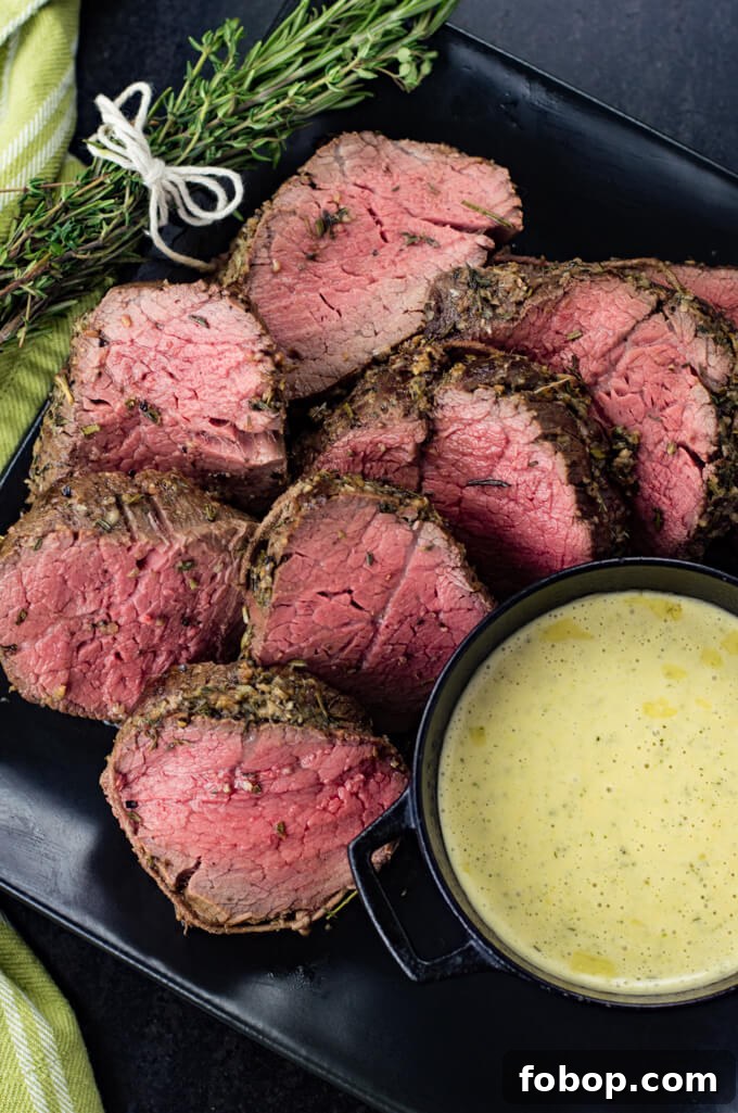 Perfect Beef Tenderloin Roast Recipe for Tender, Juicy Results 6 Sliced beef tenderloin cook rare sit on a black plate with a bundle of rosemary in the top left corner. A bowl of bearnaise sauce sits next to the slices of tenderloin.