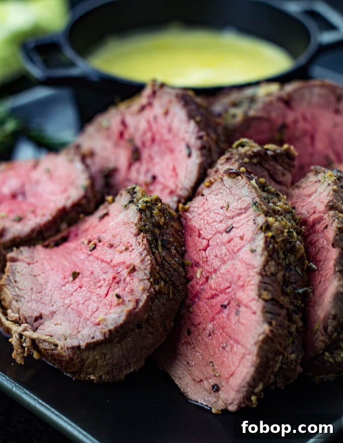 Perfect Beef Tenderloin Roast Recipe for Tender, Juicy Results 7 Rare beef tenderloin roast on a black plate with a bowl of bearnaise sauce in the background.