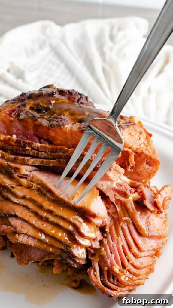 Fork piercing a spiral cut ham with brown sugar glaze.
