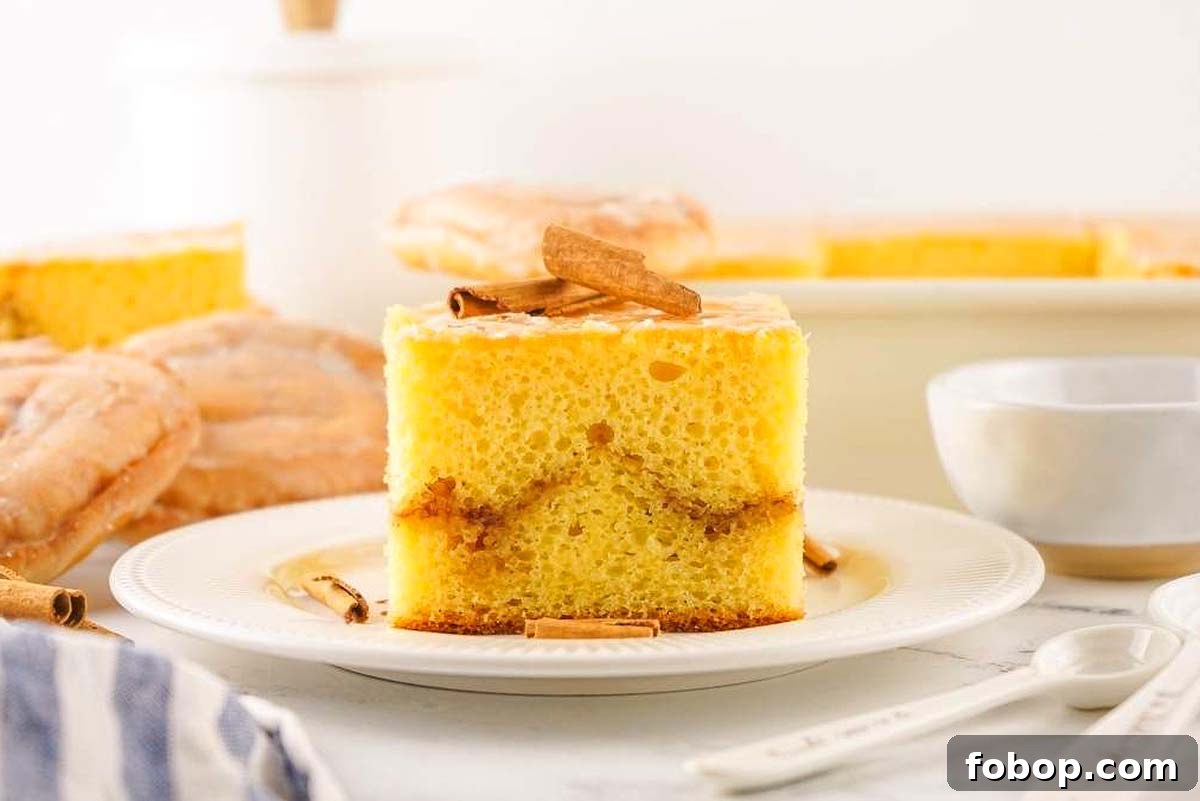 A slice of an irresistible honey bun cake recipe, sits delicately on a plate topped with aromatic cinnamon sticks. In the background, more slices accompany a rustic bowl, adding to the inviting scene.