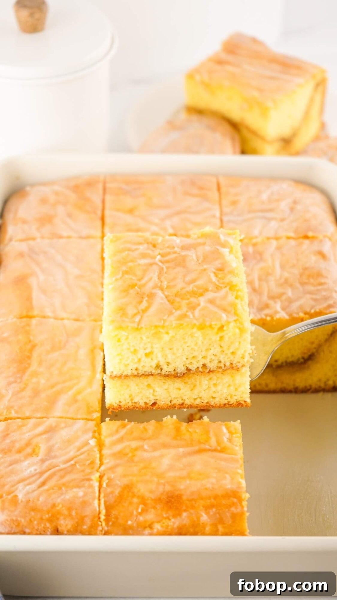 A tray of the best honey bun cake squares, with one piece being lifted by a spatula.