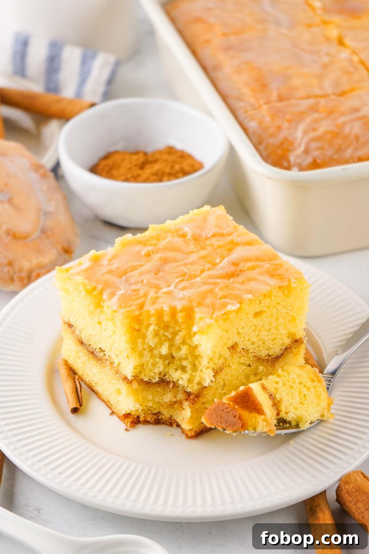 A slice of glazed cinnamon honey bun cake on a white plate with a fork.