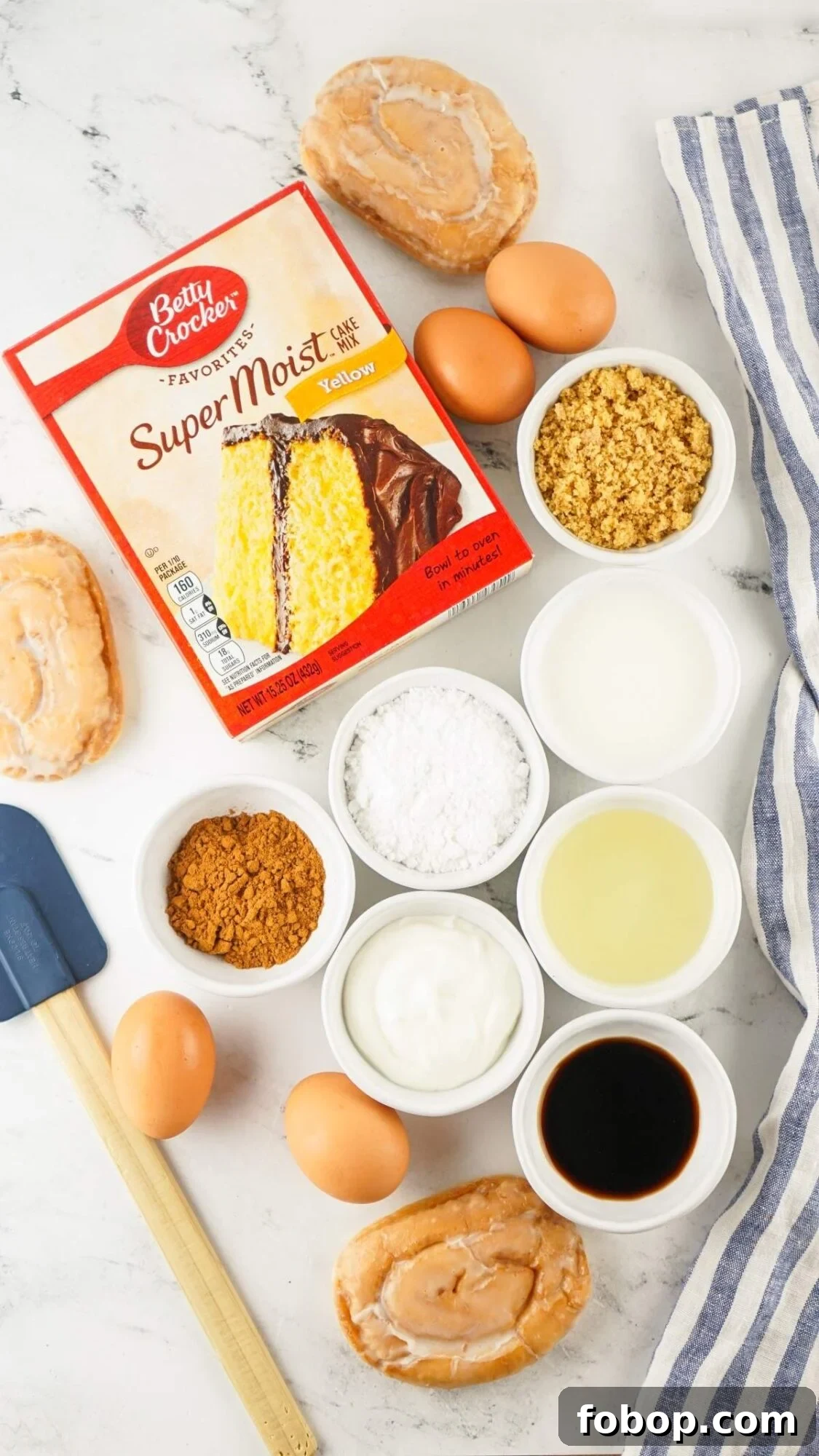 Ingredients for a honey bun cake recipe include yellow cake mix, brown sugar, eggs, yogurt, oil, vanilla extract, flour, and donuts displayed on a marble surface with a spatula and striped cloth.