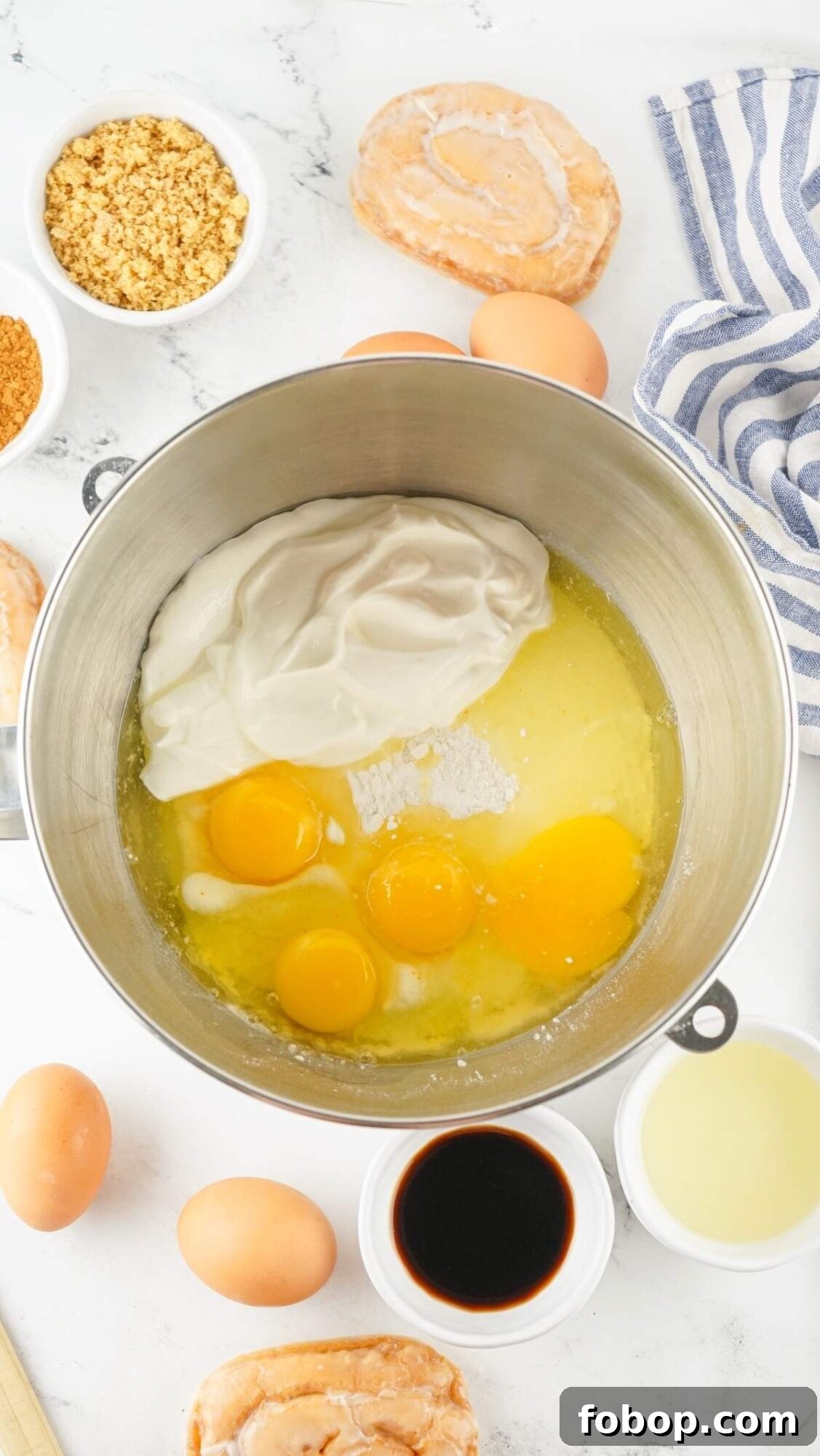 A mixing bowl with eggs, sour cream, sugar, and other ingredients sits ready to create a delectable honey bun cake recipe, surrounded by whole eggs, vanilla, and brown sugar on the countertop.