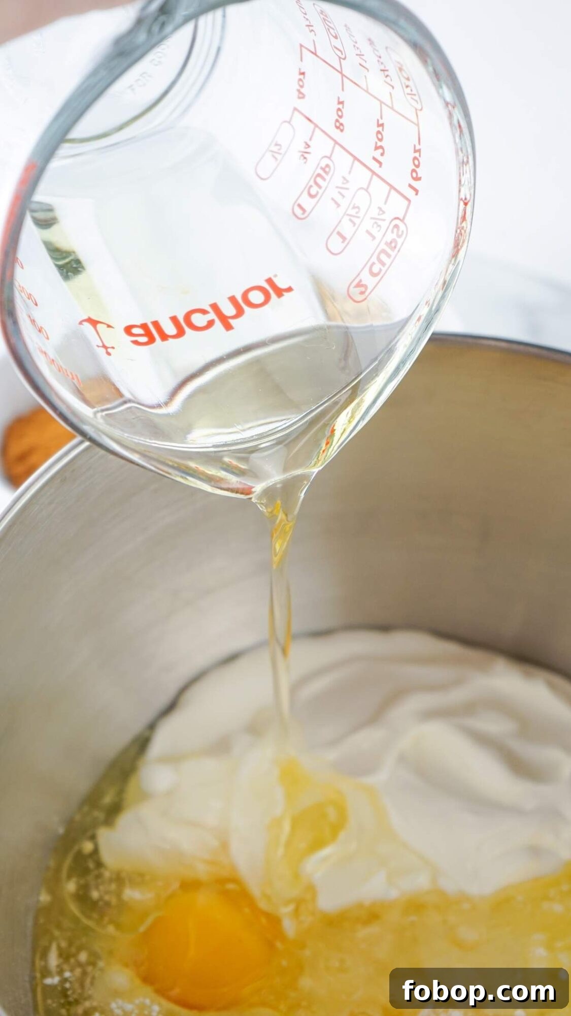 A measuring cup pours liquid into a mixing bowl containing eggs and a creamy substance, setting the stage for a delightful honey bun cake recipe.