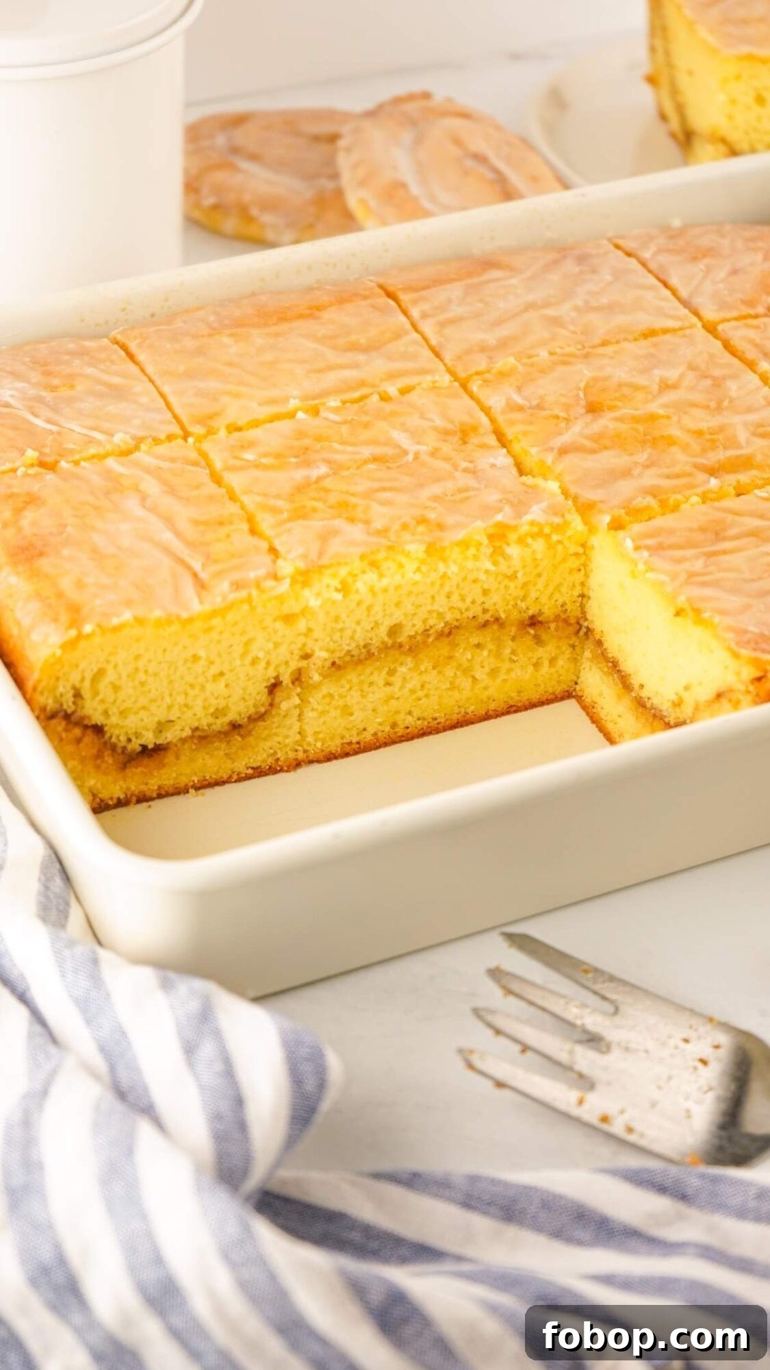 A tray of delicious honey bun cake with icing, one piece missing. A striped cloth and fork are nearby, tempting a taste.
