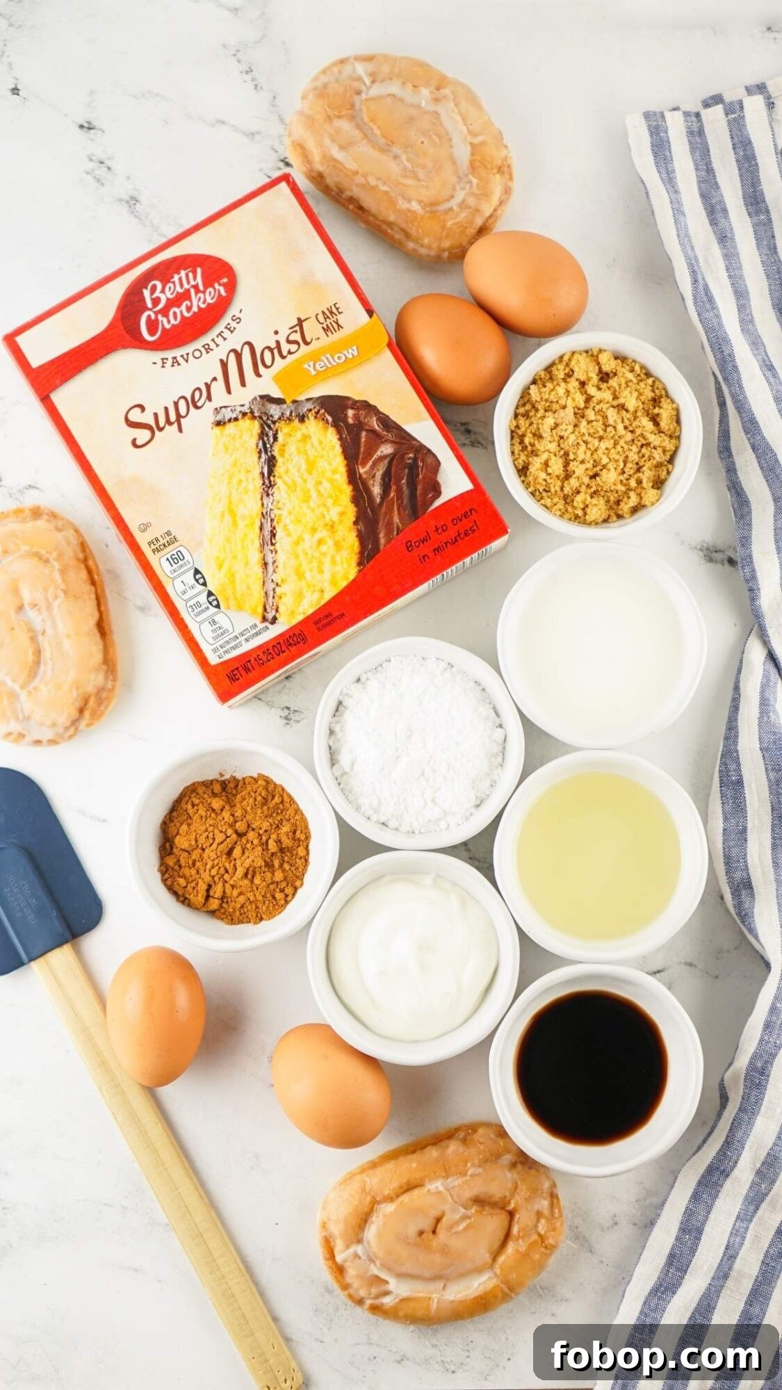 Ingredients for a honey bun cake recipe include yellow cake mix, brown sugar, eggs, yogurt, oil, vanilla extract, flour, and donuts displayed on a marble surface with a spatula and striped cloth.