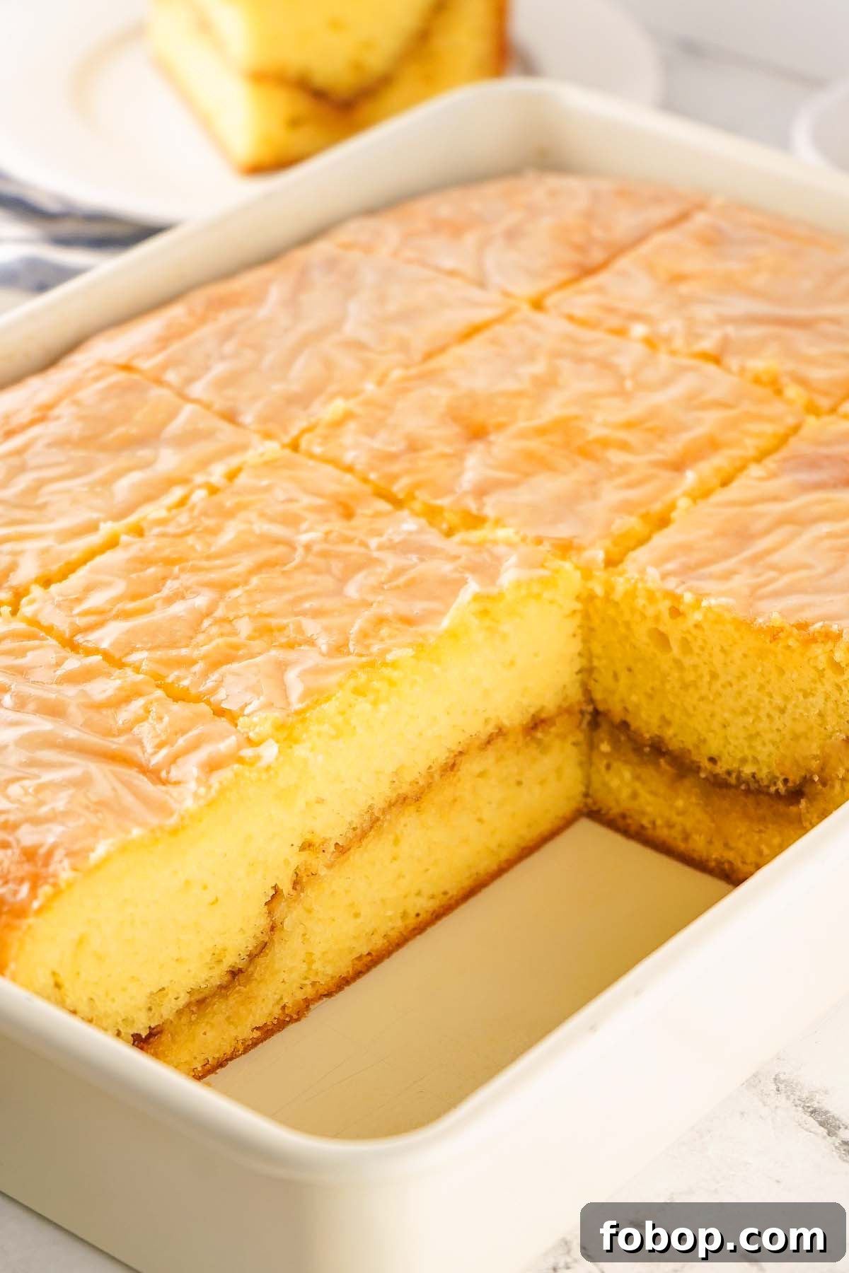 A rectangular cake mix honey bun cake with icing, is sliced into squares in a baking dish, with one piece missing from the corner.