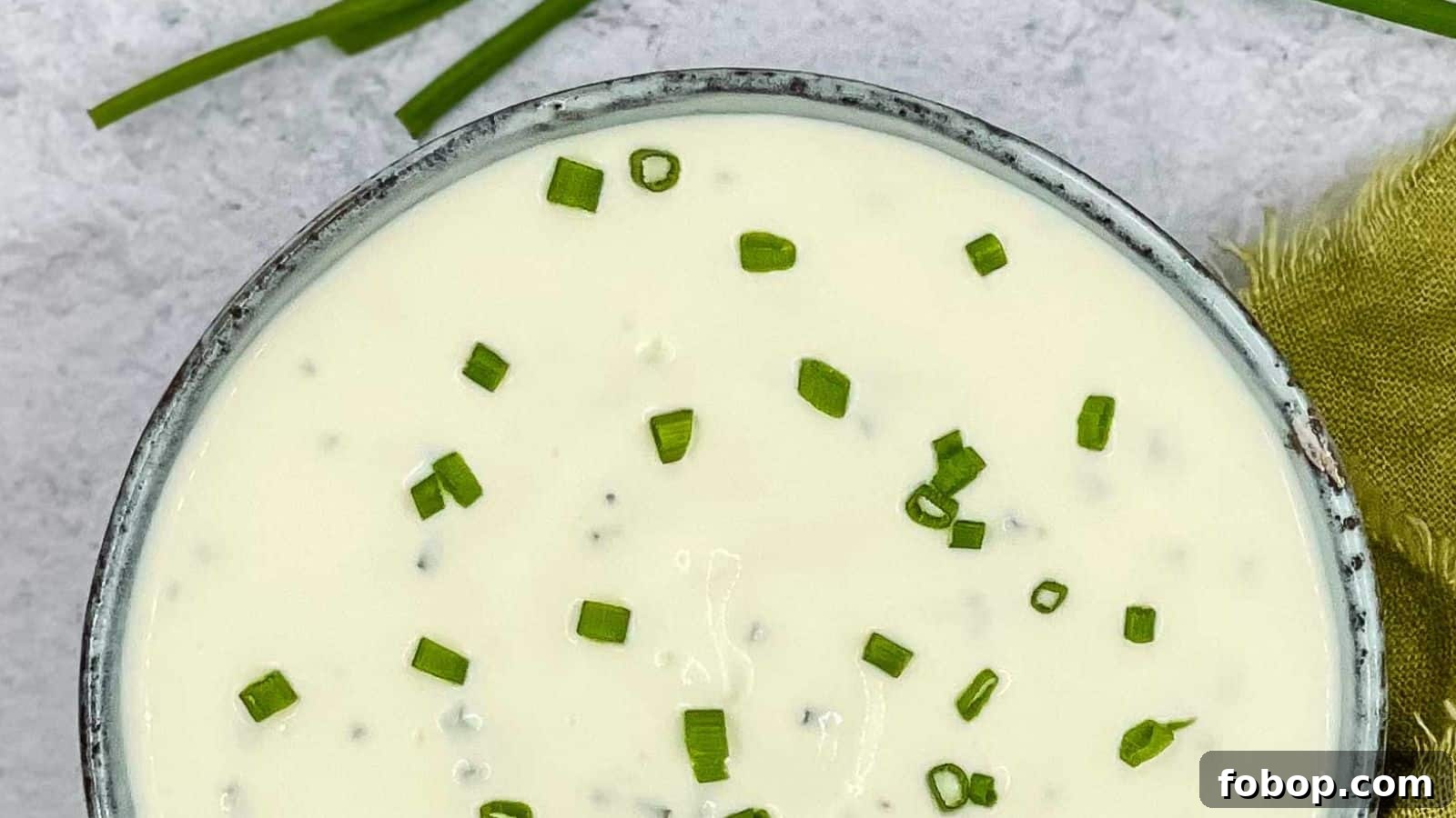 Sour cream and chives dressing in a bowl with chives and lemon around it.