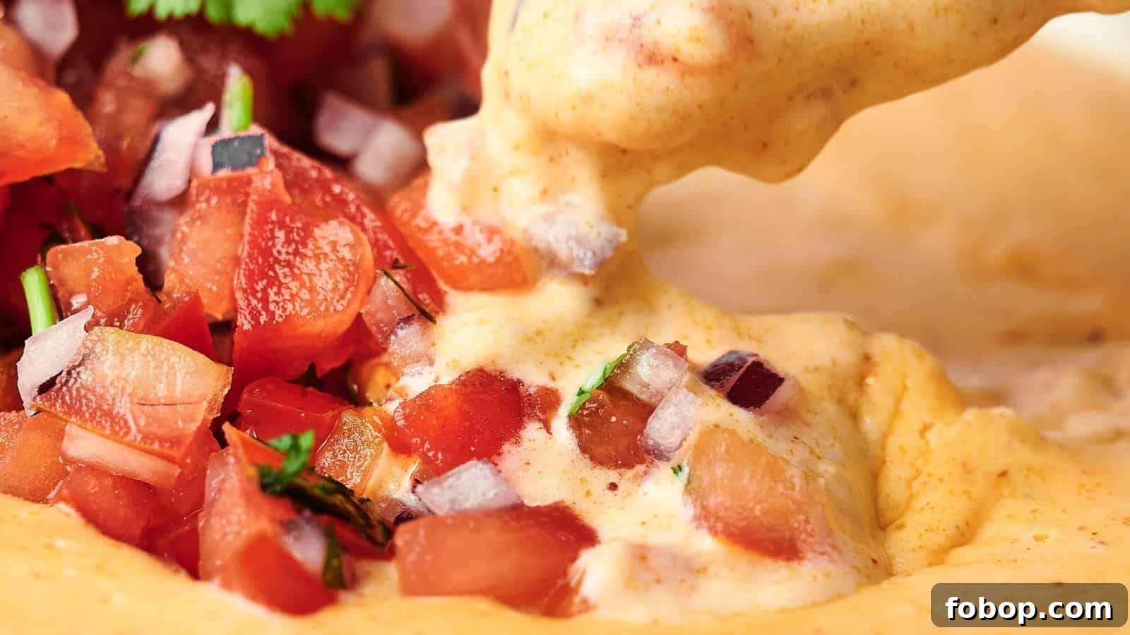 Close-up of creamy cheese dip being poured over chopped tomato salsa with diced onions and cilantro.