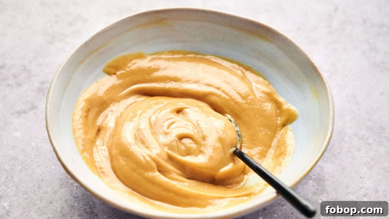 A bowl of smooth, creamy peanut butter with a hint of Chick-fil-A sauce and a spoon inside.
